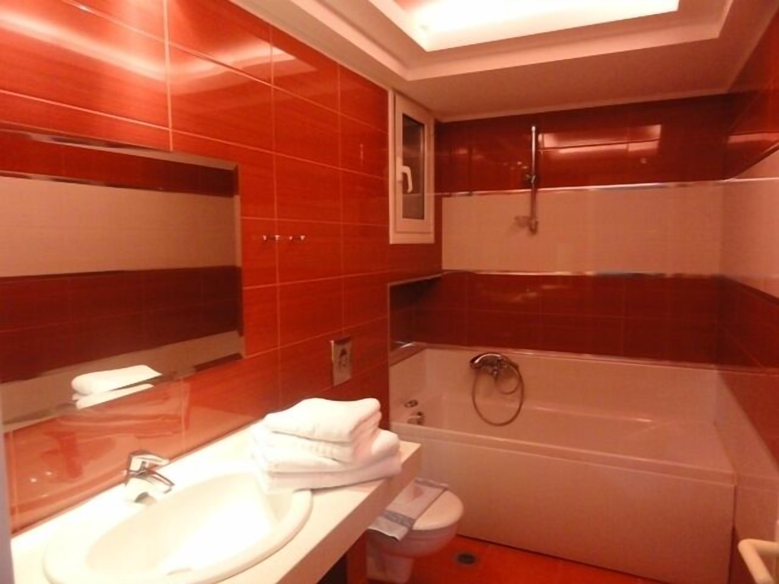Un baño con azulejos rojos, un lavamanos blanco, un espejo, un inodoro y una bañera.