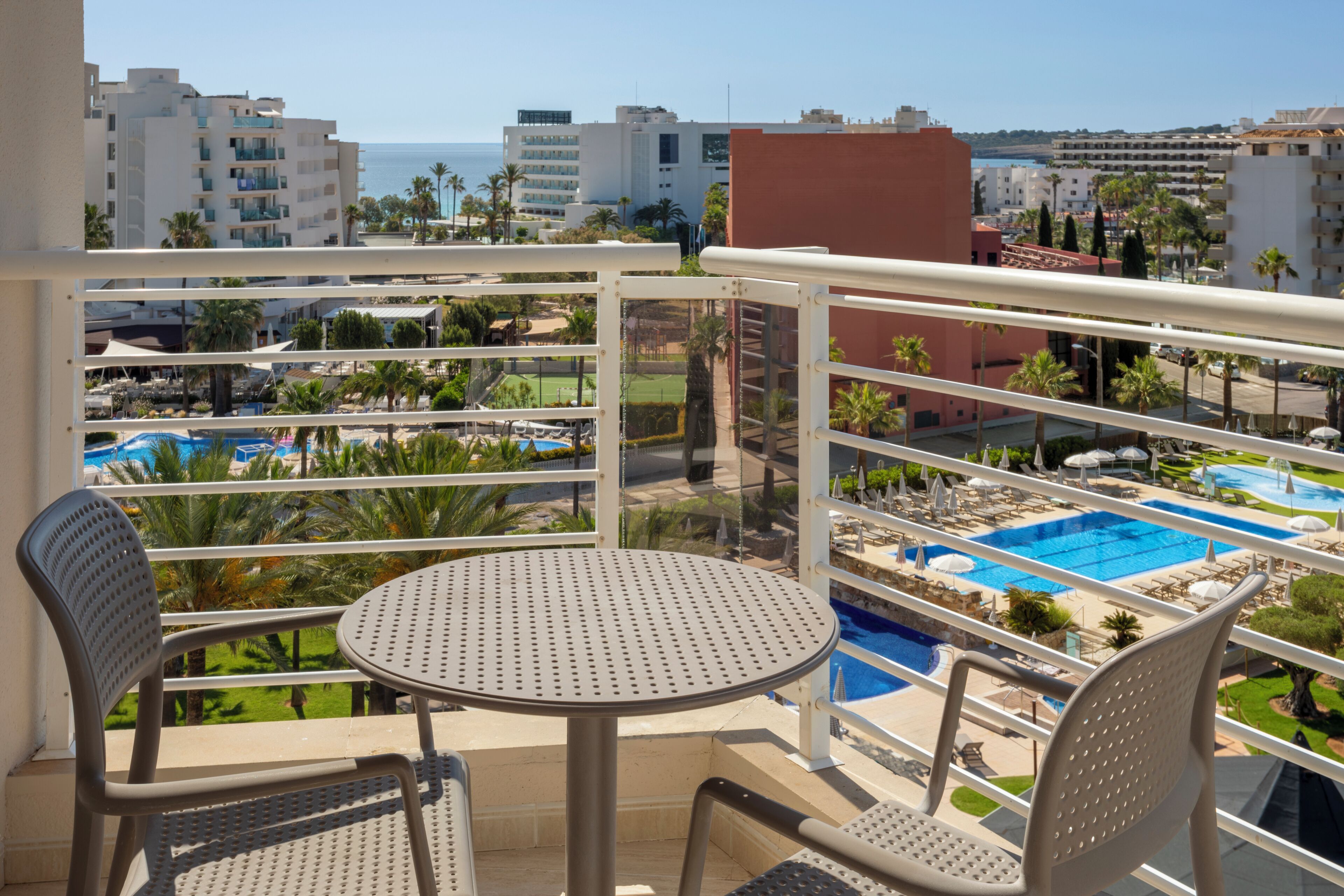 A balcony with a view of a swimming pool, palm trees, and hotel buildings.
