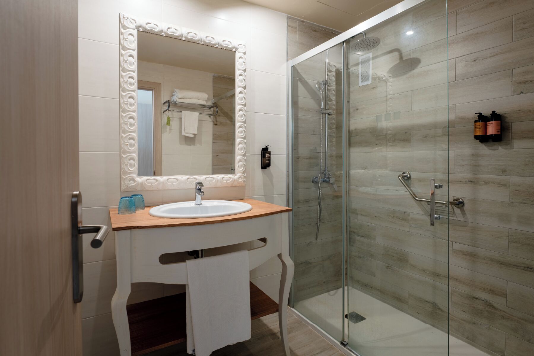A bathroom with a glass shower enclosure, a white sink, and a mirror with a decorative frame.