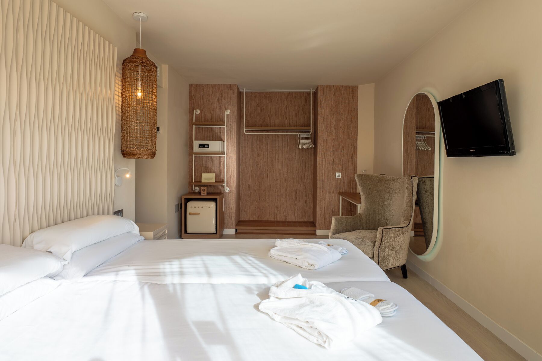 Una habitación de hotel con cama, una silla, televisor, armario y un refrigerador pequeño.