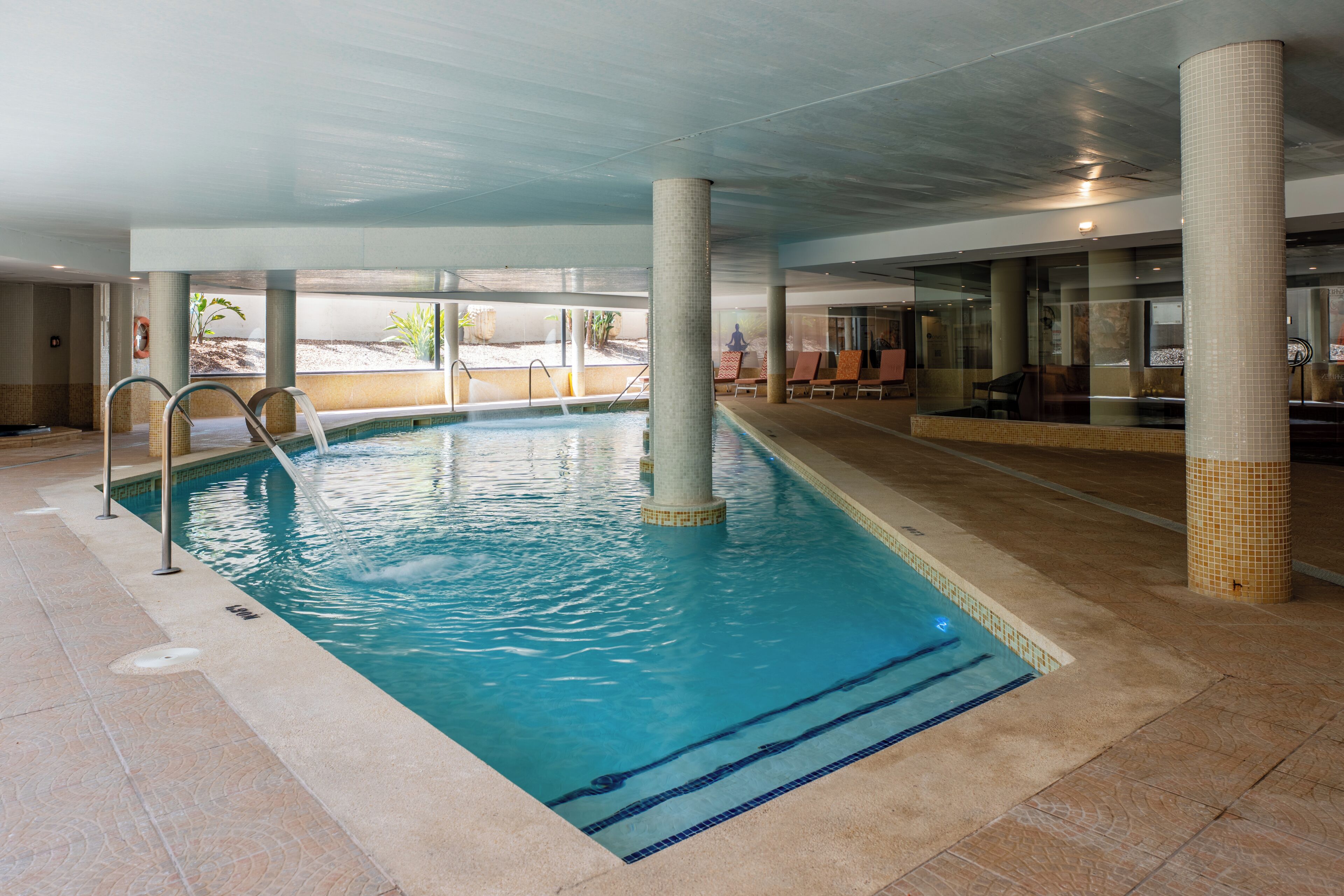 An indoor swimming pool with clear water, tiled floor, and columns.