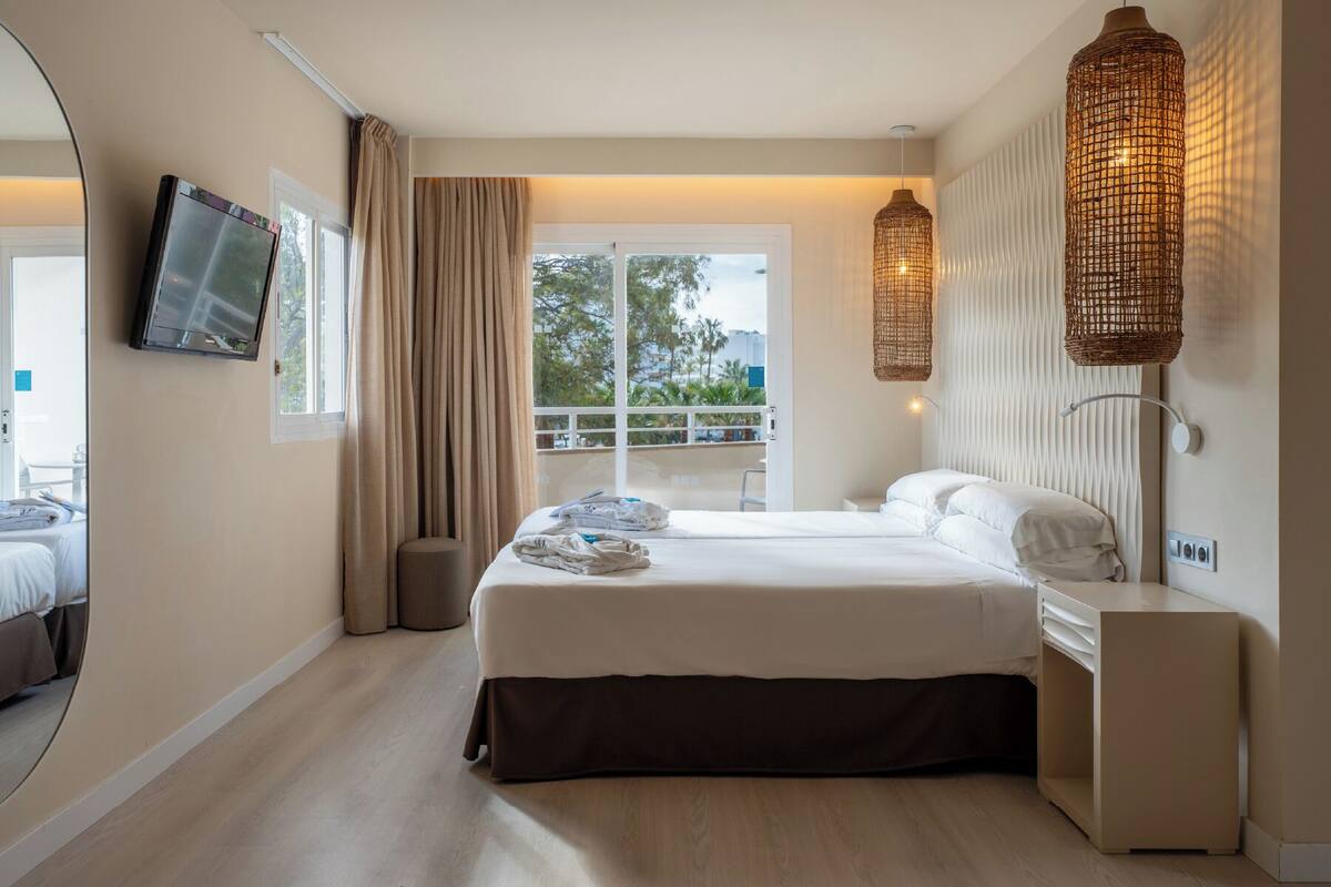Ein Hotelzimmer mit einem Bett, einem Fernseher, einem Balkon mit Geländer und Korblampen.