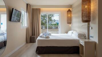A hotel room with a bed, a television, a balcony with a railing, and wicker lamps.