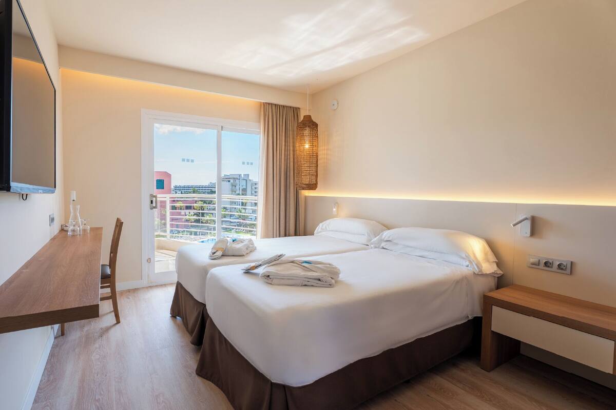 Ein Hotelzimmer mit Bett, Nachttischen, Schreibtisch und Fernseher.