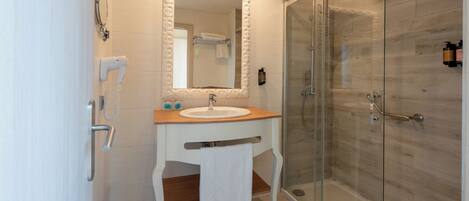 A modern bathroom with a glass-enclosed shower, a white sink with a wooden countertop, and a large mirror with an ornate frame.