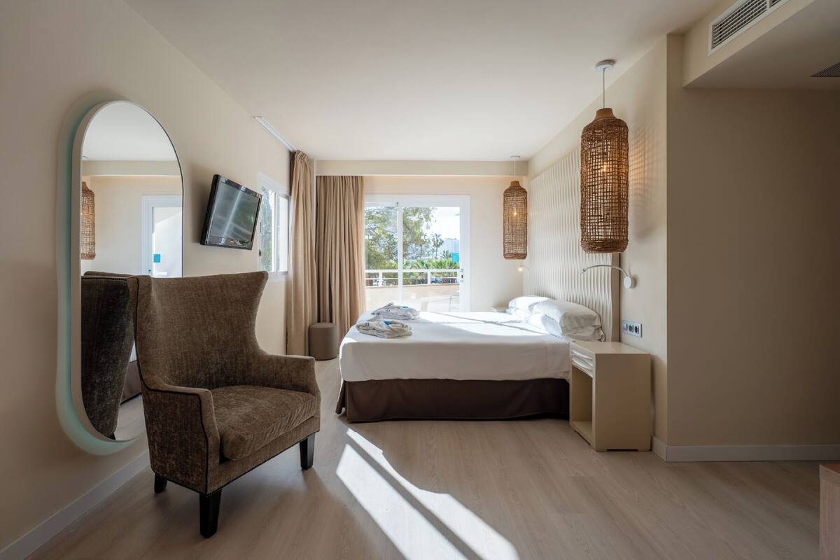 Ein Hotelzimmer mit Bett, Sessel, Fernseher und einem großen Fenster.