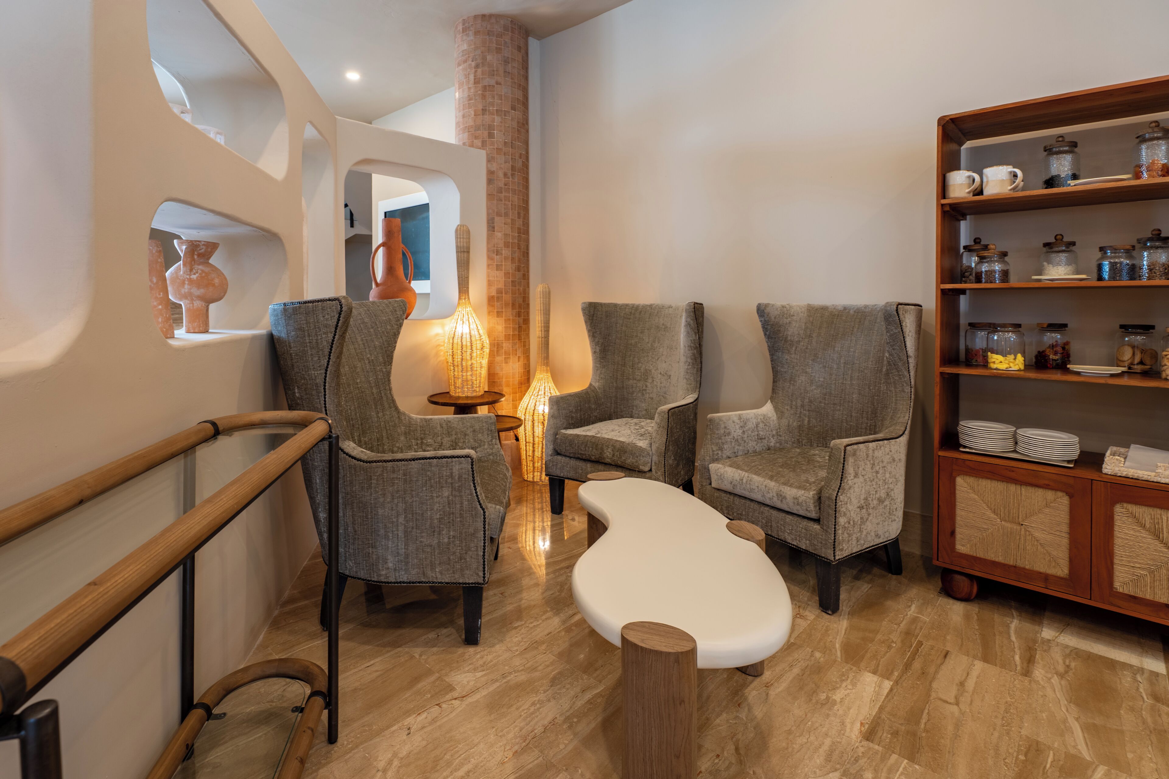 Un intérieur moderne avec un banc en bois, des chaises grises à revêtement rembourré, une bibliothèque en bois et une colonne recouverte de carreaux.
