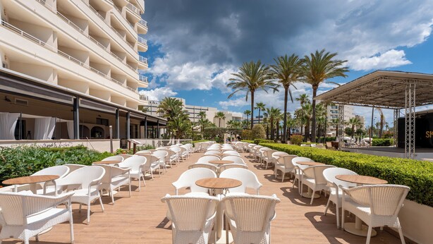 A hotel patio with outdoor seating, palm trees, and a building with balconies. - Cala Millor Garden, Adults Only (Sant Llorenc des Cardassar)