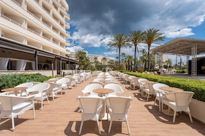 A hotel patio with outdoor seating, palm trees, and a building with balconies. - Cala Millor Garden, Adults Only (Sant Llorenc des Cardassar)