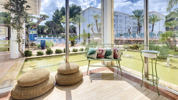 A poolside area with a view of a pool, lounge chairs, and a small table. - Aparthotel Green Garden (Capdepera)