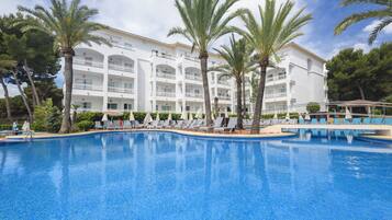Un hôtel doté d’une piscine, de palmiers et d’un bâtiment blanc orné de nombreux balcons.