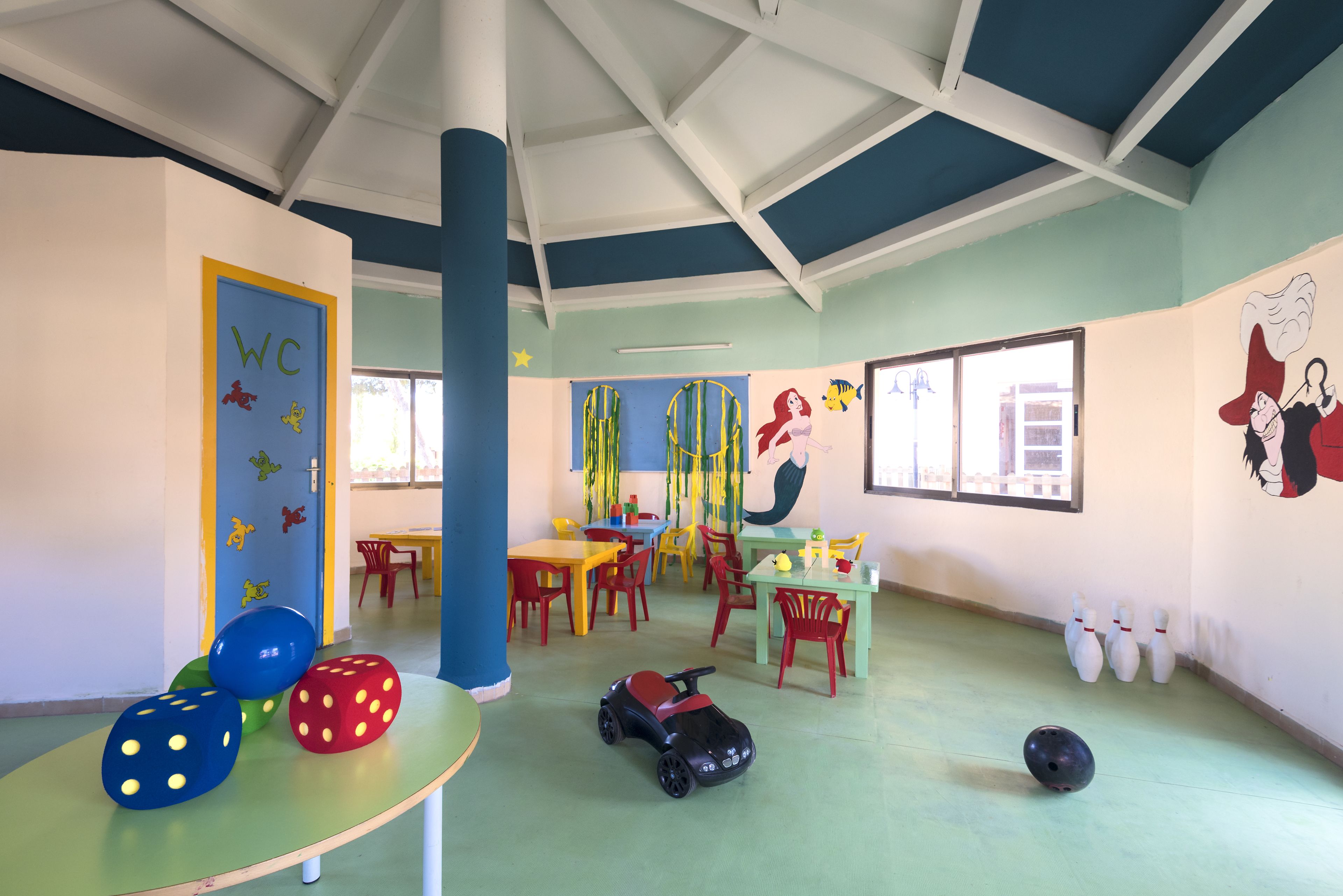 Un salón de juegos infantil de colores vivos, con mesas, sillas y juguetes educativos.