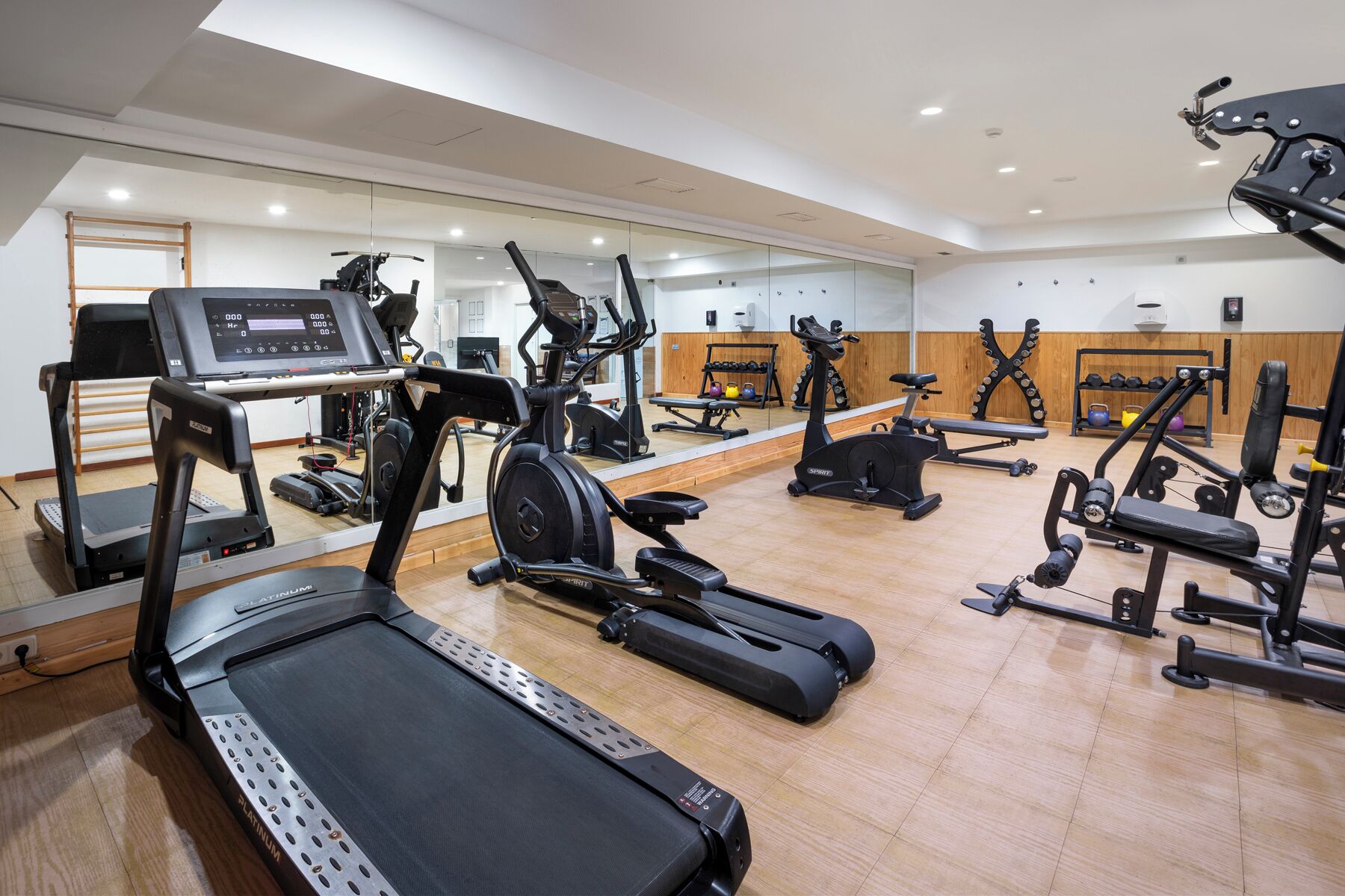 Un gimnasio con diversos equipos de ejercicio, incluyendo cintas de correr, elípticas y máquinas de pesas.