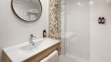 A modern bathroom with a white sink, a round mirror, a shower with a glass door, and a tiled wall with a mosaic pattern.