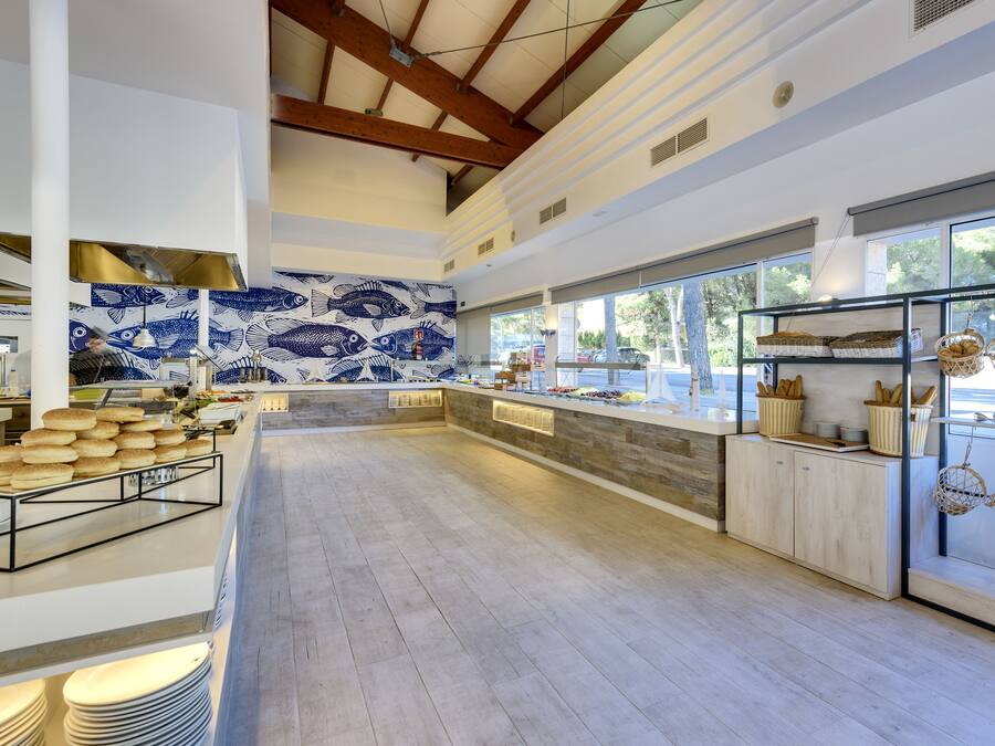 Amplia zona de buffet con una larga barra, un salpicadero de azulejos con motivos de peces y cestas de pan a la derecha.