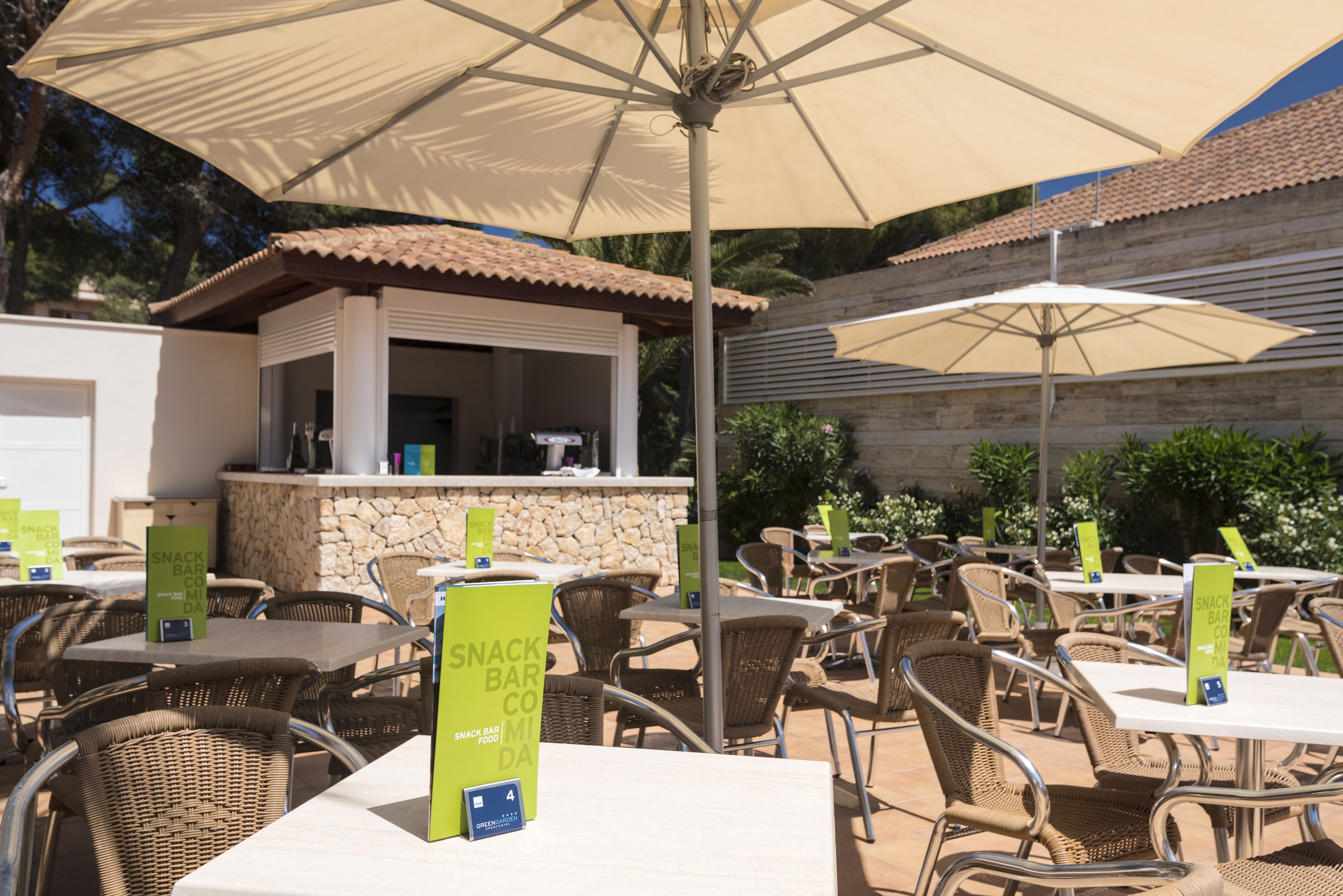 An outdoor dining area with tables and chairs, a snack bar, and umbrellas providing shade.