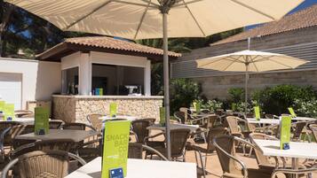 An outdoor dining area with tables and chairs, a snack bar, and umbrellas providing shade.