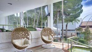 Two wicker chairs with cushions on a balcony with a view of trees and a building. - Aparthotel Green Garden (Capdepera)
