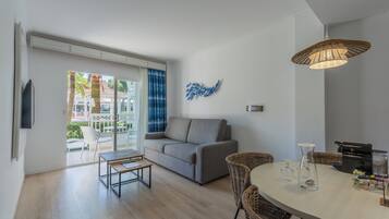 Una sala moderna con un sofá gris, una mesa de comedor con sillas de mimbre y un ventanal con vistas a palmeras.