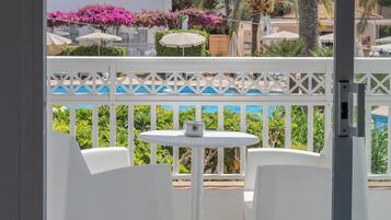 Un balcon avec des chaises blanches et une petite table, donnant sur un espace piscine agrémenté de parasols et d’une végétation luxuriante.