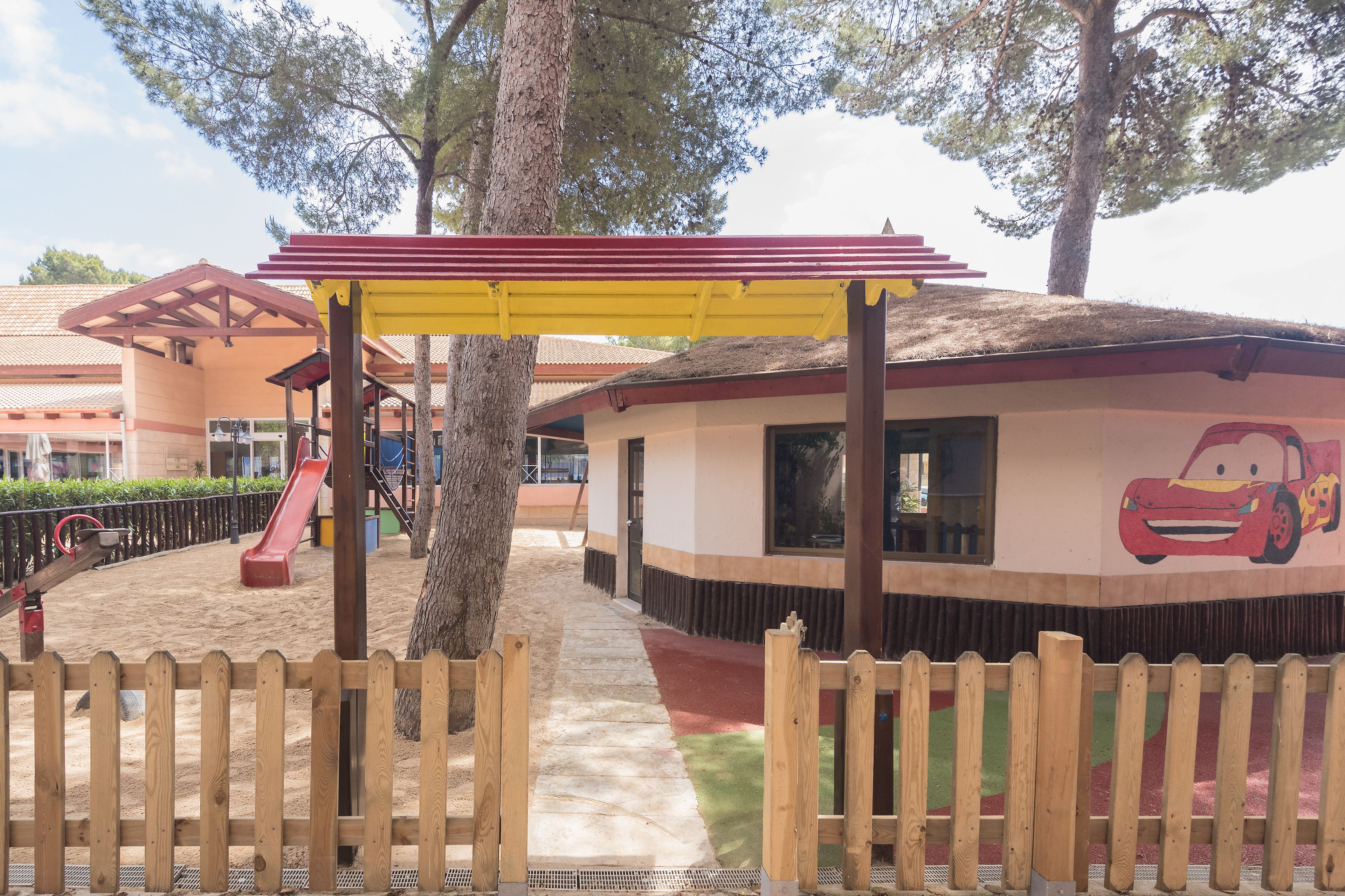 Un parque infantil con un tobogán, una estructura para escalar y una zona cubierta con un mural de coches.