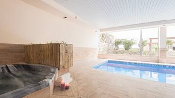 Un espace bien-être comprenant un jacuzzi, un banc en bois et une piscine.