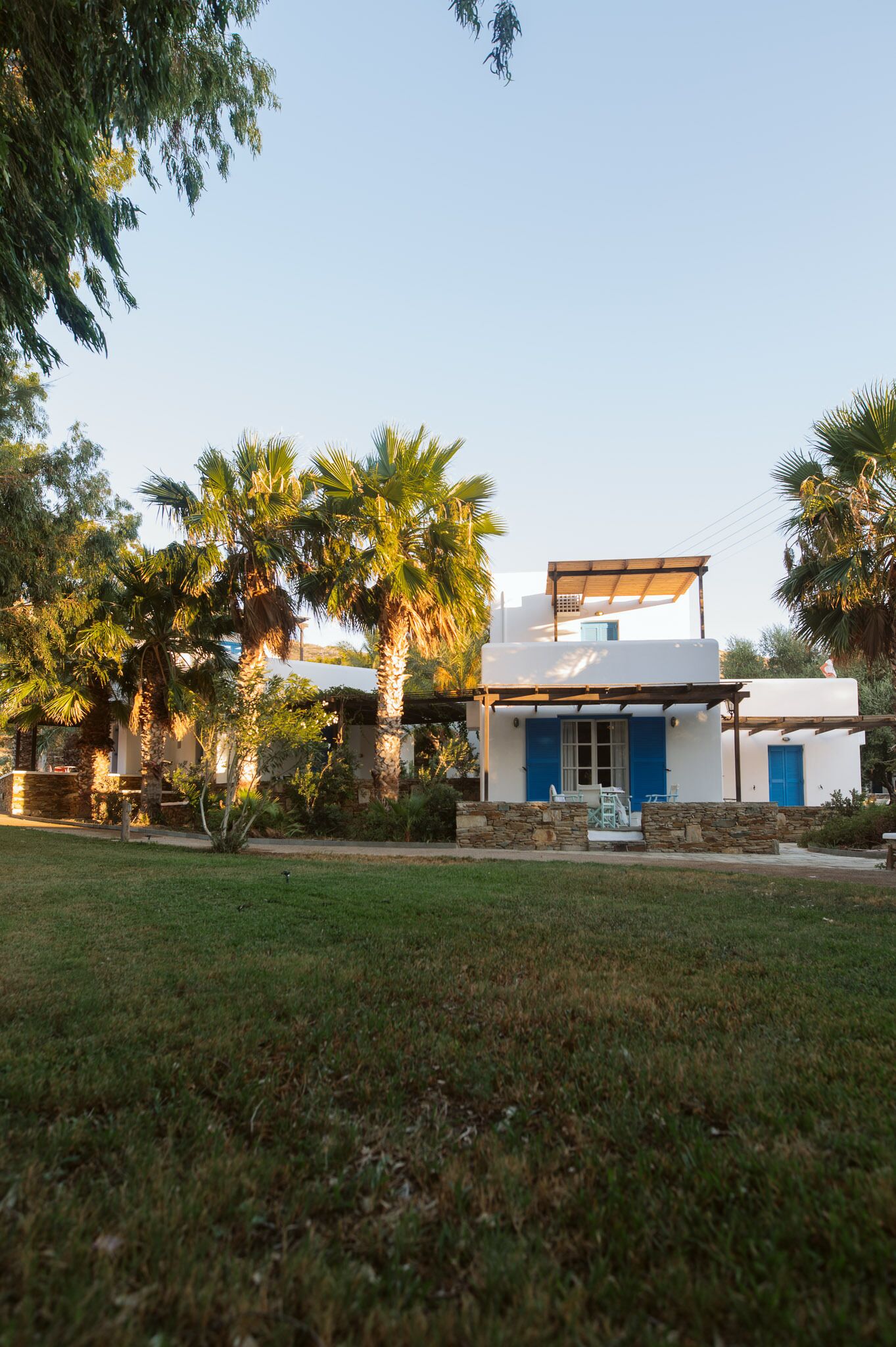 A modern house with a white exterior and blue accents, surrounded by lush greenery and palm trees.