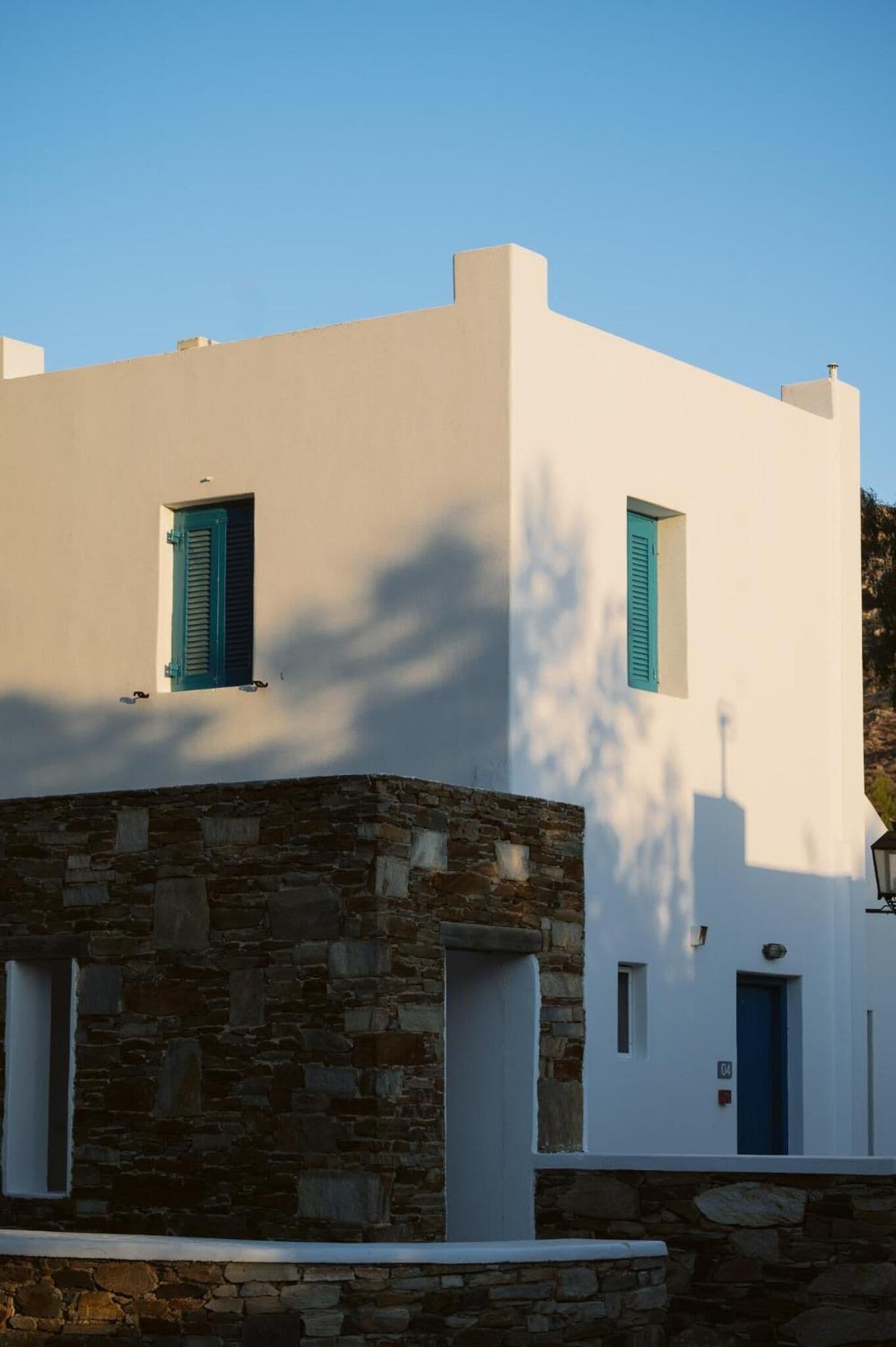 A white building with two windows, one with a blue shutter.