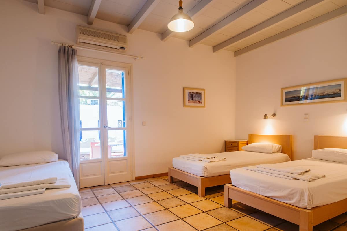 Habitación de hotel con dos camas individuales, un ventanal con cortinas, una puerta que da al exterior y un ventilador de techo.