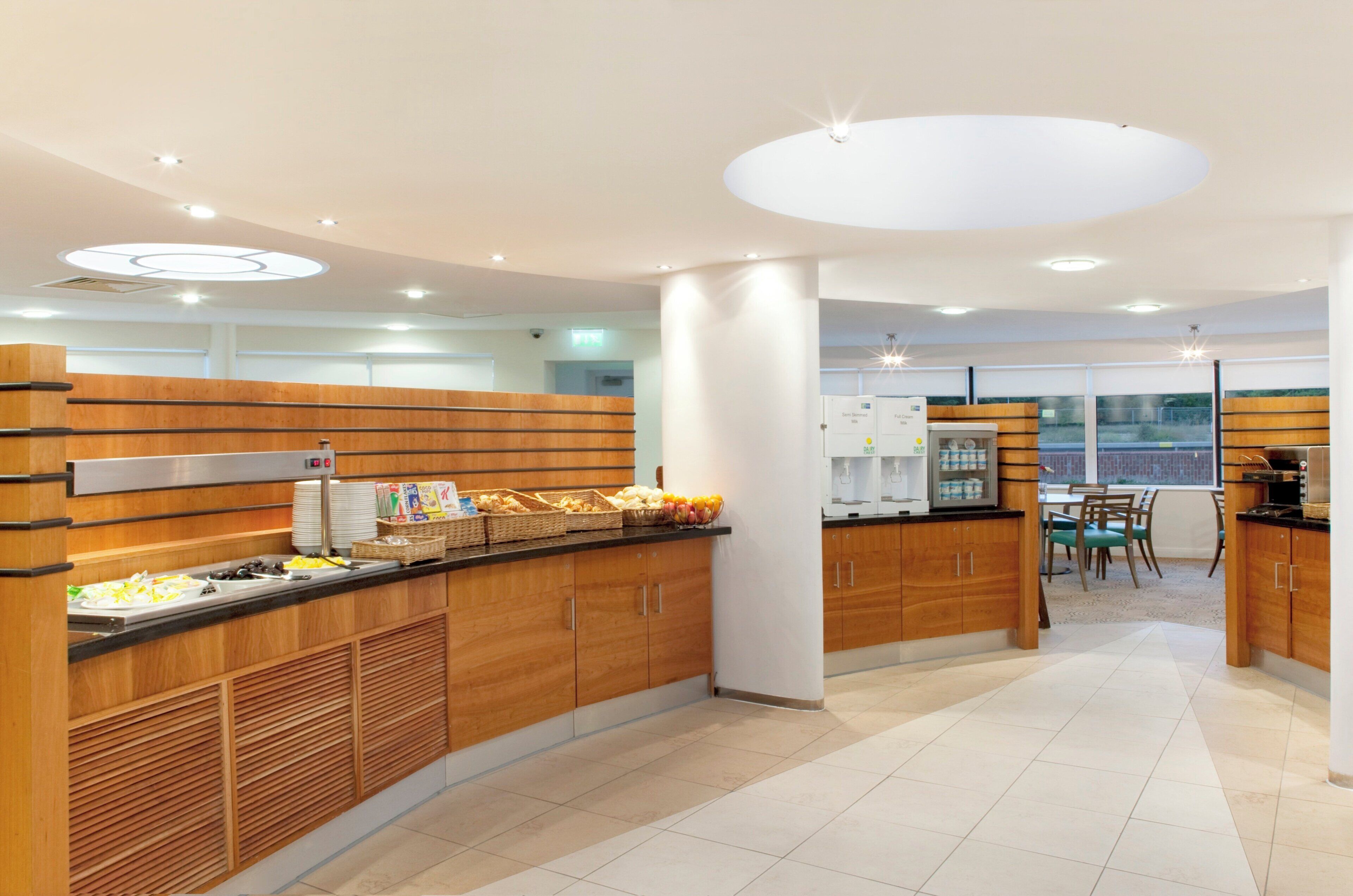 A modern kitchen area with wooden cabinets, a buffet counter with food items, and a dining area with a table and chairs.