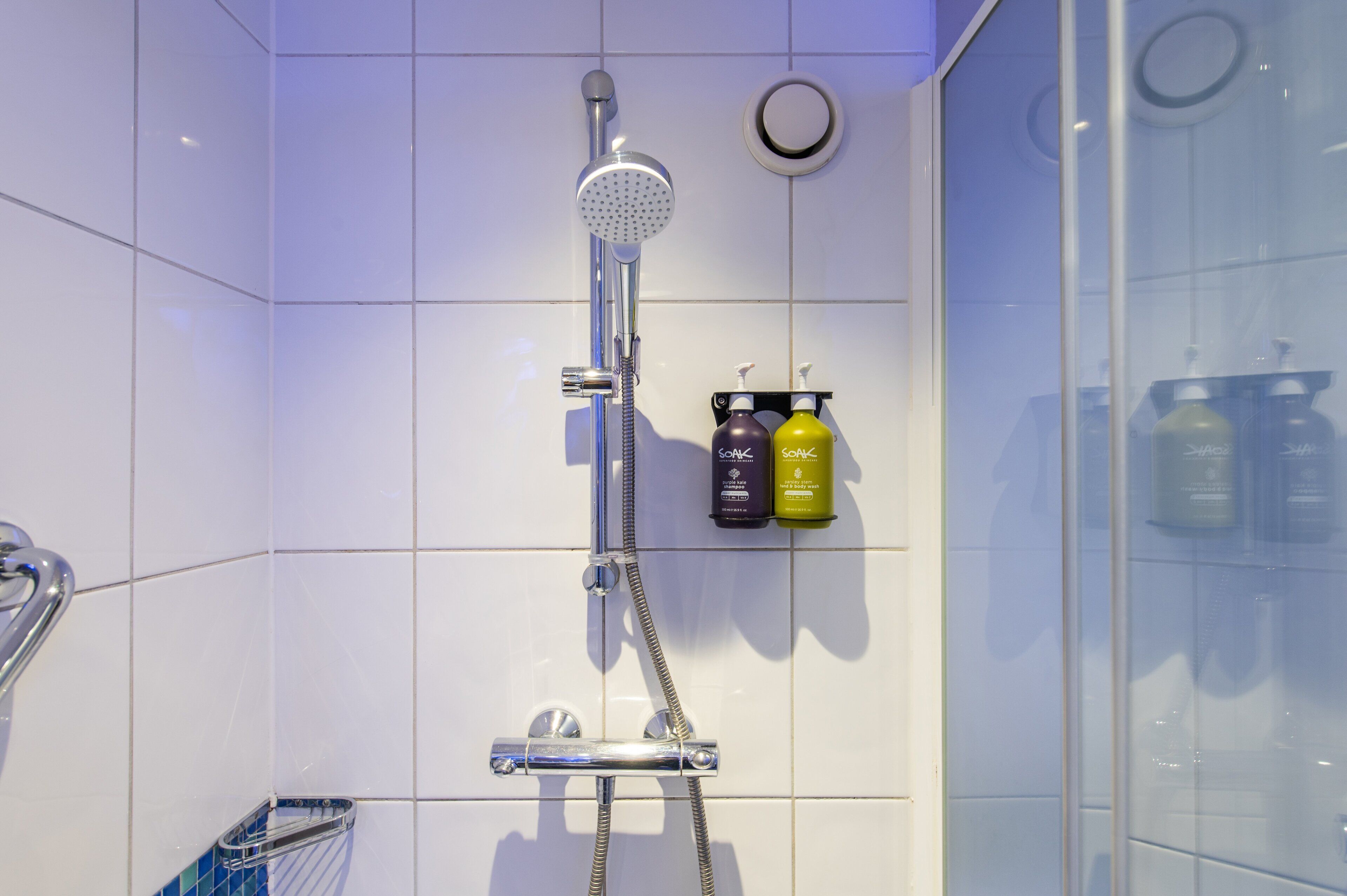 A shower with a handheld showerhead, a handheld shower attachment, and two bottles of shampoo on a shelf.