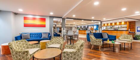 A spacious lobby with a blue sofa, patterned chairs, and a reception desk.