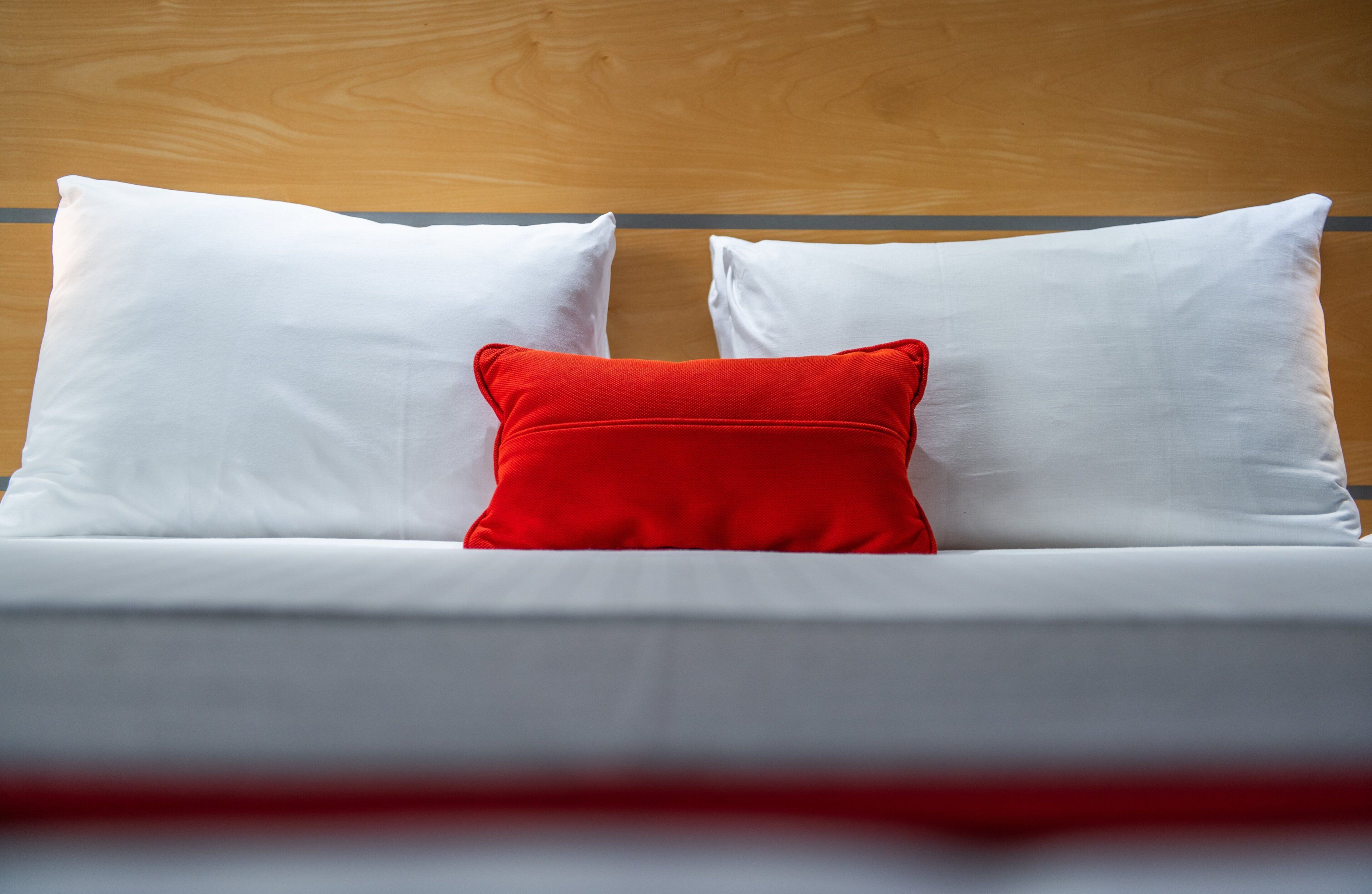Un letto con biancheria bianca e un cuscino rosso.