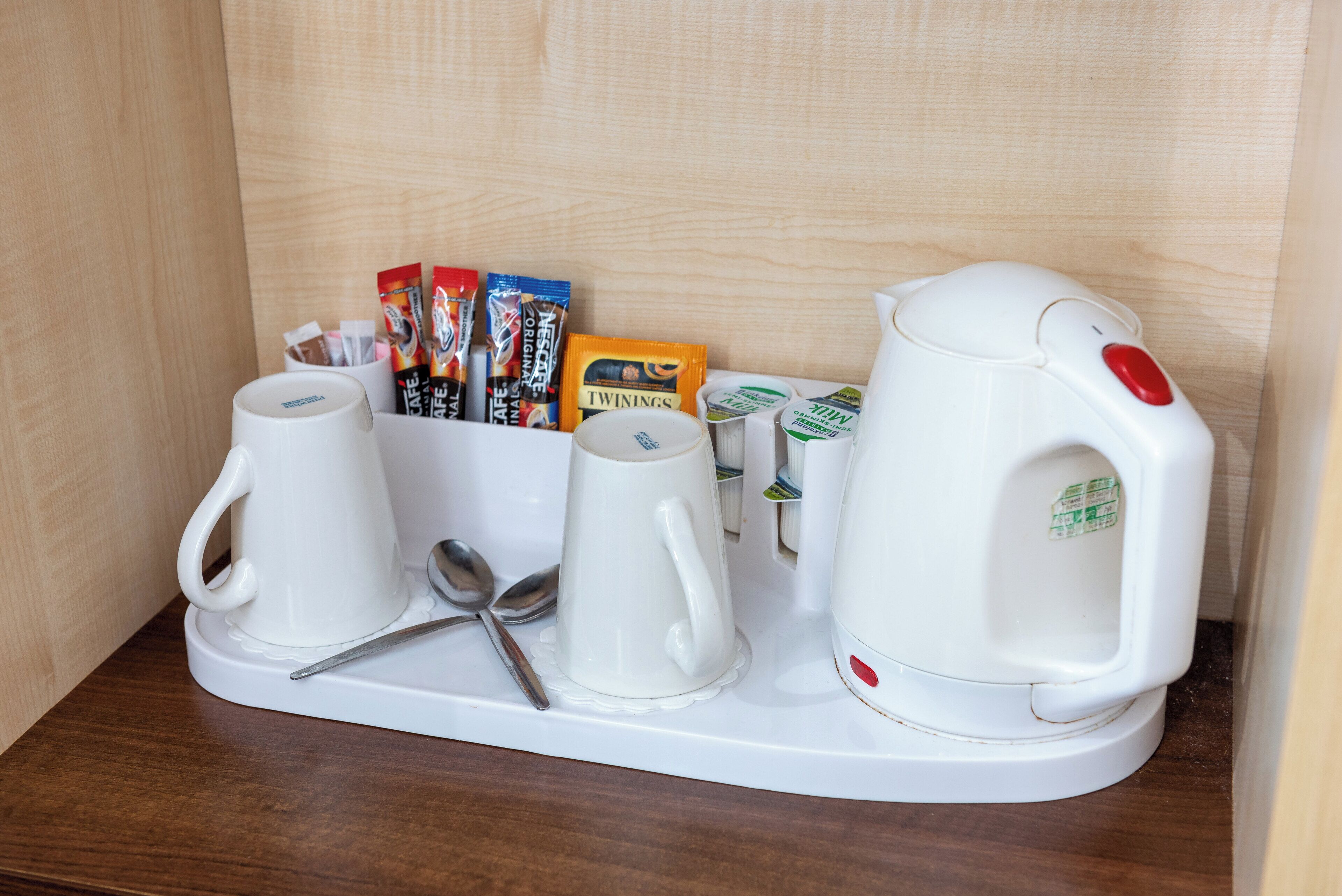 Un coin café comprenant deux tasses à café blanches, une cuillère, une bouilloire et divers dosettes de café.