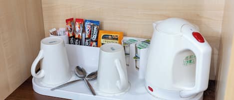A coffee station with two white coffee cups, a spoon, a kettle, and various coffee pods.