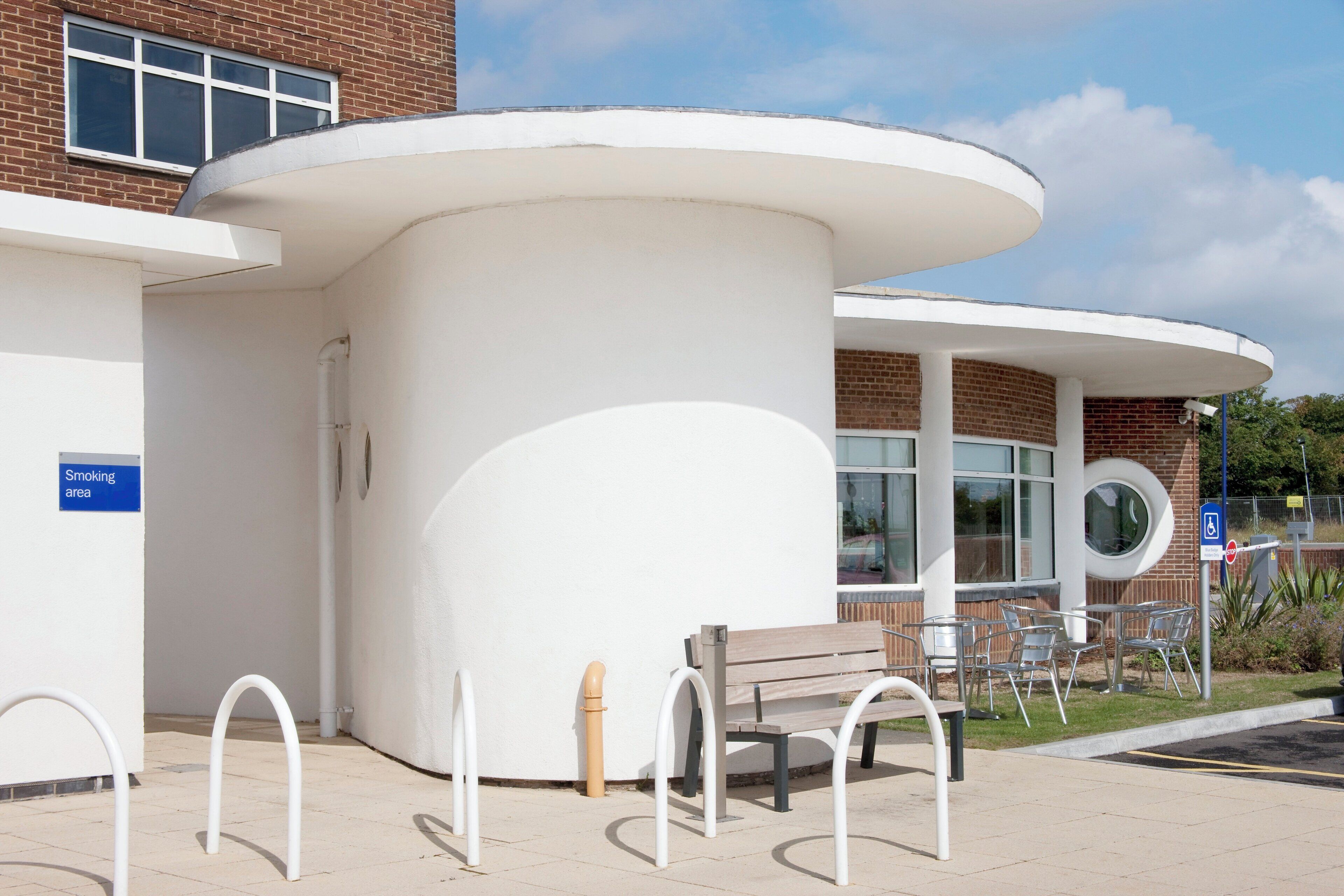 A building with a white exterior, a bench, and a smoking area sign.