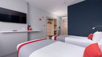 Habitación de hotel con dos camas, un televisor fijado a la pared, un armario y un estante con objetos.