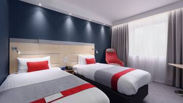Habitación de hotel con dos camas, una silla roja, un cabecero de madera y un ventanal con cortinas.
