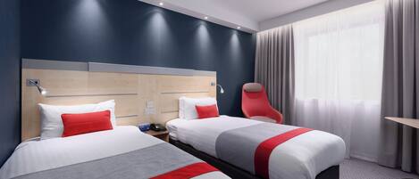 A hotel room with two beds, a red chair, a wooden headboard, and a large window with curtains.