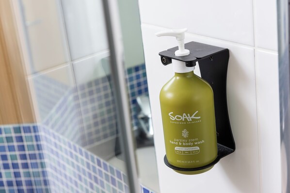 A bottle of Soak Parsley Stem Hand & Body Wash mounted on a wall in a bathroom with blue and white tiles.