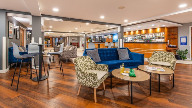 A hotel lobby with a blue sofa, patterned chairs, a bar area, and wooden flooring. - Holiday Inn Express Ramsgate - Minster by IHG (Ramsgate)