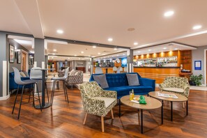 A hotel lobby with a blue sofa, patterned chairs, a bar area, and wooden flooring.