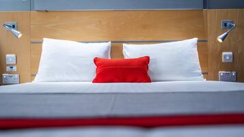 A neatly made bed with white and red pillows, a wooden headboard, and bedside lamps.
