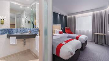 Una habitación de hotel con baño, dos camas, un espejo y una ventana con cortinas.