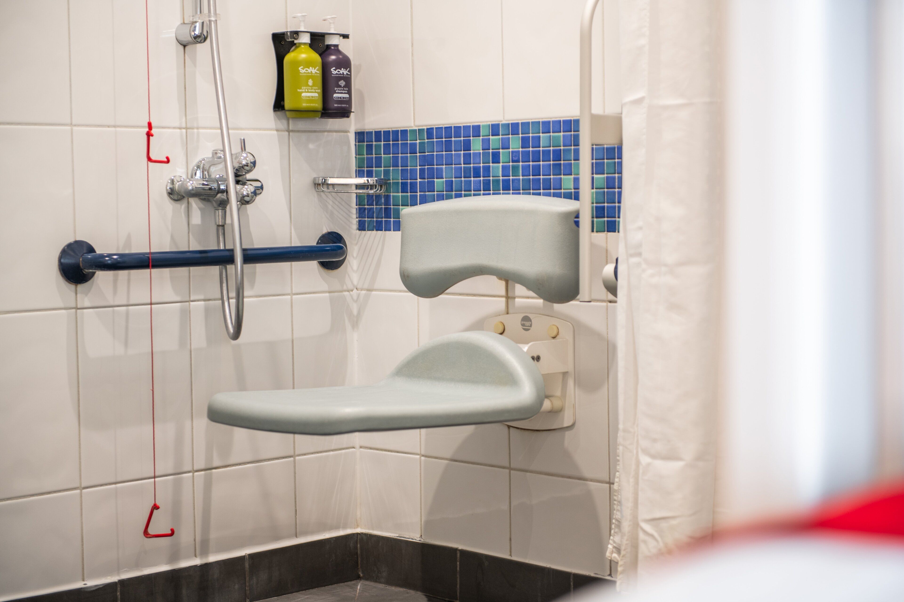 A bathroom with a wheelchair-accessible shower, grab bars, and a tiled wall.