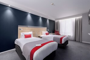 A hotel room with two beds, a desk, and a large window with curtains.