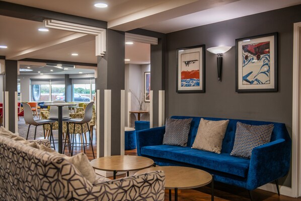 A modern lounge area with a blue sofa, patterned cushions, and a round wooden table.