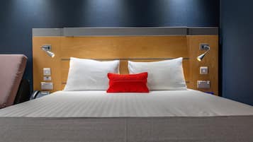 A neatly made bed with white and red pillows, a wooden headboard, and bedside lamps.