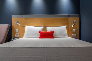 A neatly made bed with white and red pillows, a wooden headboard, and bedside lamps. - Holiday Inn Express Ramsgate - Minster by IHG (Ramsgate)
