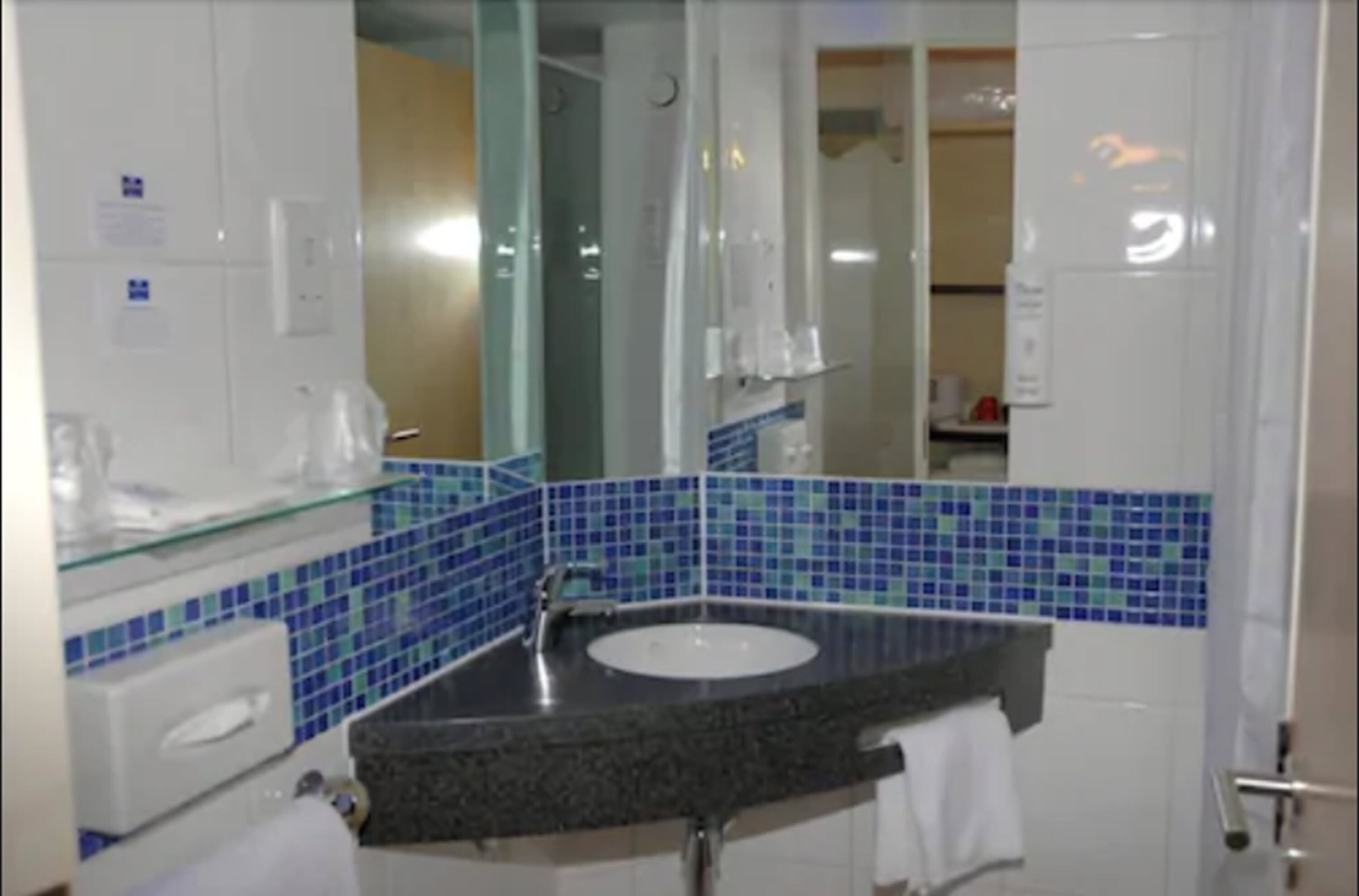 A bathroom with a glass-enclosed shower, a sink with a dark countertop, and blue-tiled walls.